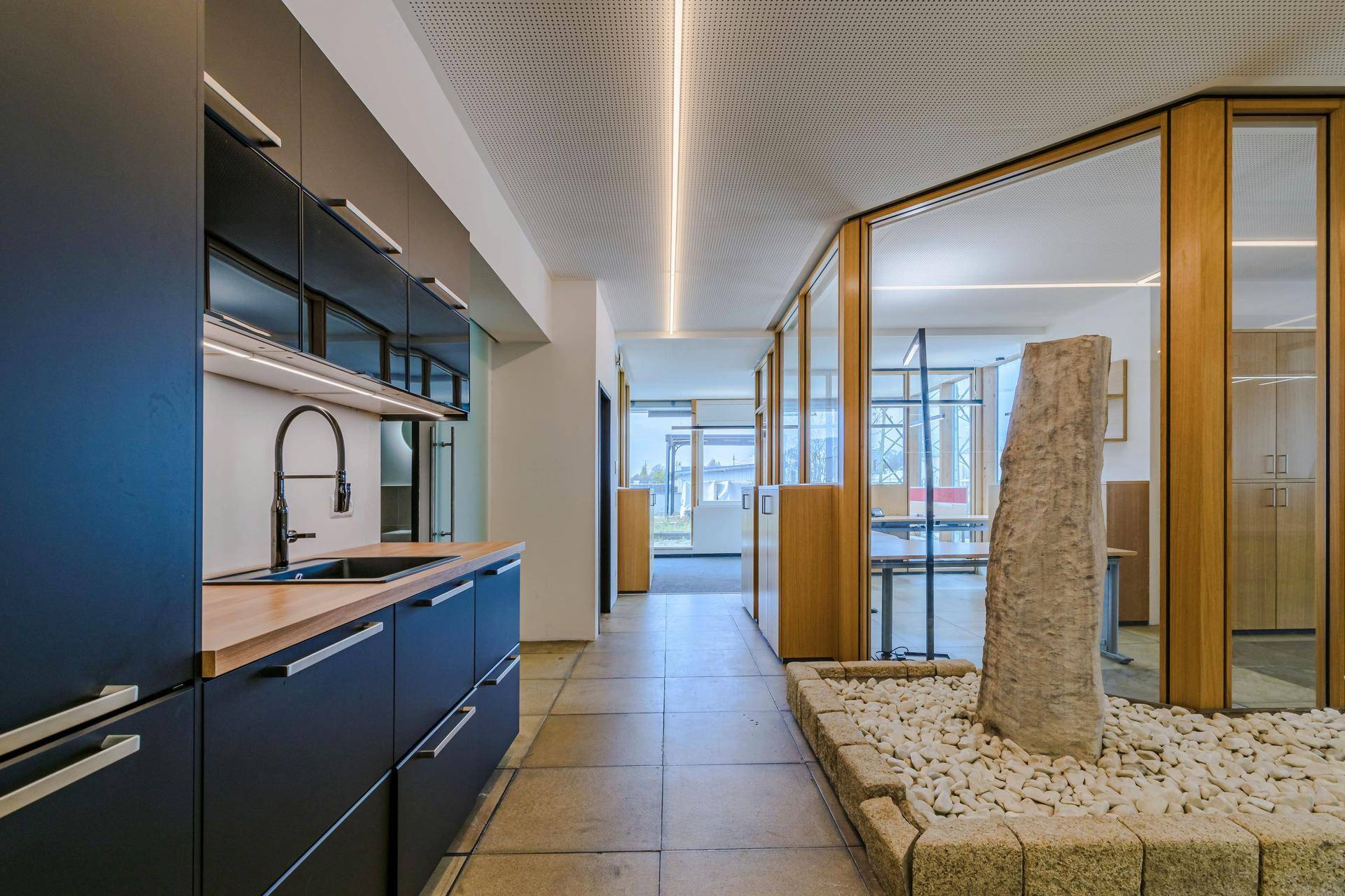 Moderne Küchenzeile mit dunklen Schränken und Holztheke, daneben ein dekorativer Steinbrunnen.