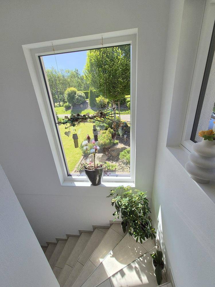 Heller Treppenaufgang mit großem Fenster, das einen Blick auf den gepflegten Garten bietet.