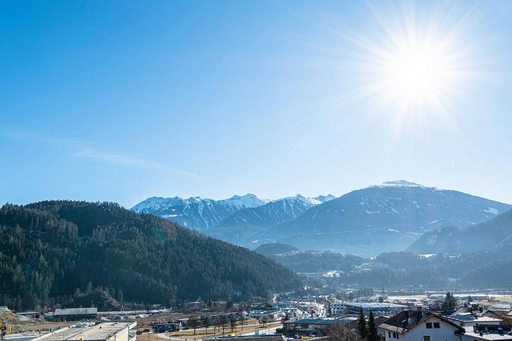 Sonniger Ausblick auf die bewaldeten Hügel und die schneebedeckten Gipfel in der Ferne.