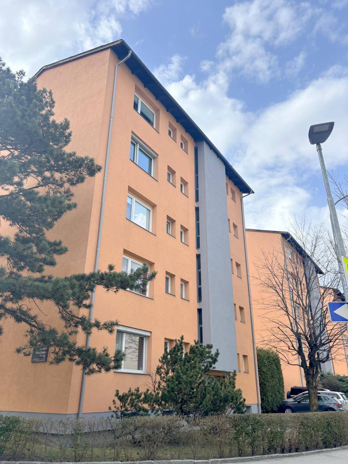 Mehrstöckiges Wohngebäude mit orangefarbener Fassade und blauen Akzenten unter bewölktem Himmel.