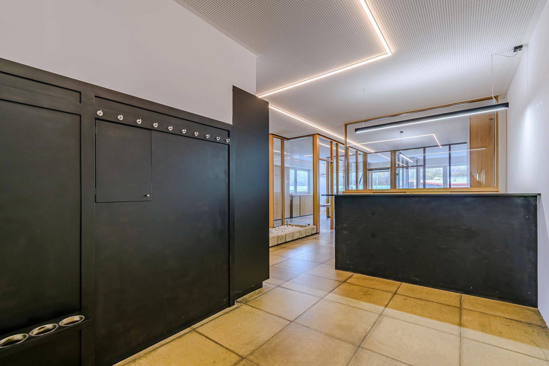 Empfangsbereich mit dunkler Theke und Garderobe, führt zu hellen Büroräumen mit Glaswänden.