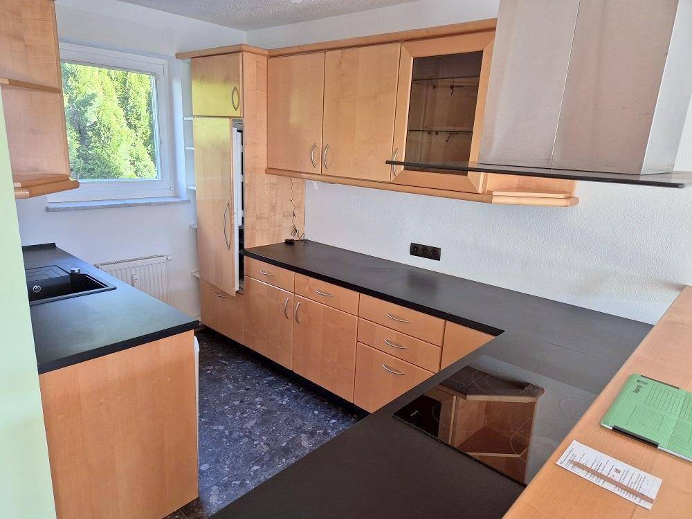 Funktionale Küche mit Holzschränken, dunkler Arbeitsplatte und Fenster mit Blick ins Grüne.