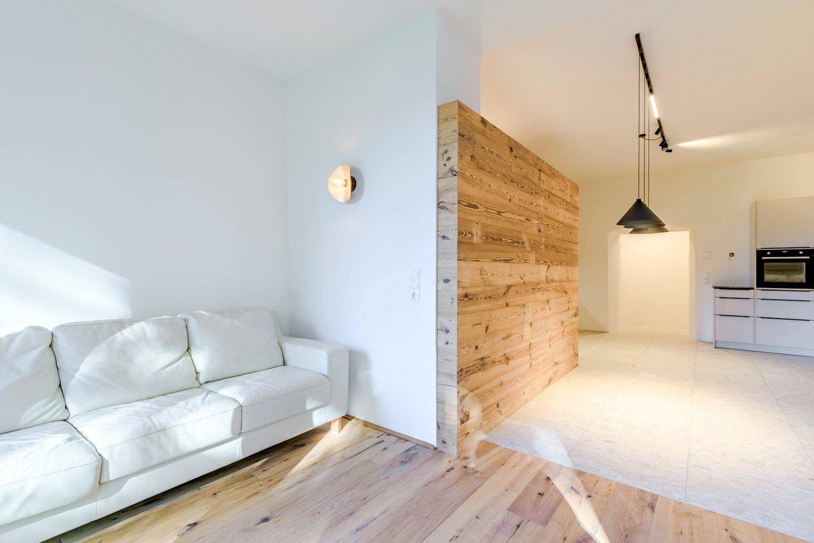 Heller Wohnbereich mit weißem Sofa, Holzwand und Blick auf die offene Küche mit modernen Elementen.