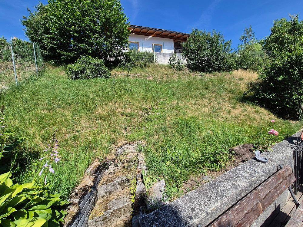 Großer, leicht geneigter Gartenbereich mit Rasenfläche und Blick auf ein weiteres Gebäude.