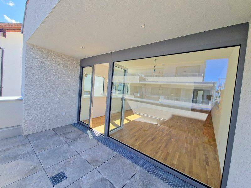 Geräumige Terrasse mit Fliesenboden und großzügiger Glasfront zum lichtdurchfluteten Innenbereich des Hauses.