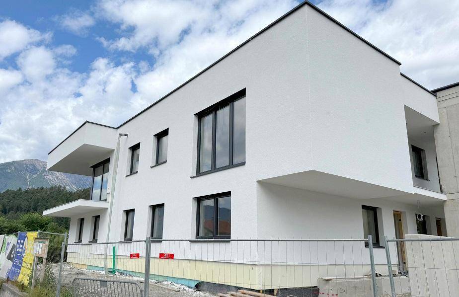 Seitenansicht des modernen Neubaus mit weißen Wänden, schwarzen Fenstern und Balkonen.