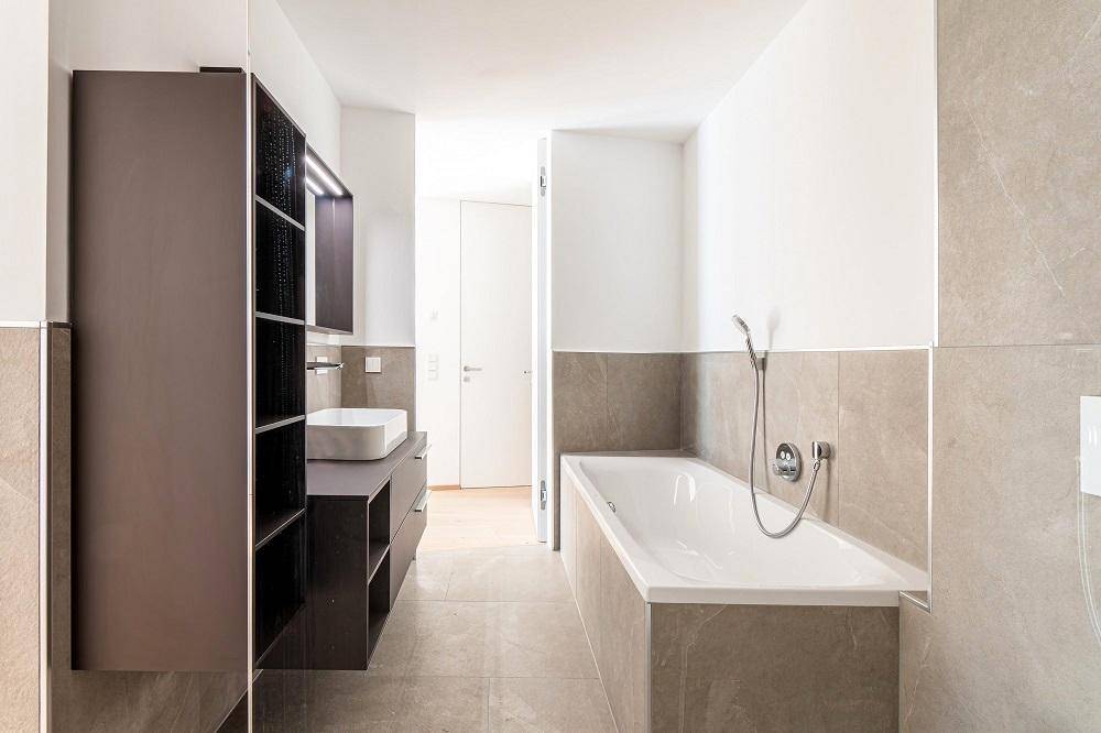 Helles Badezimmer mit Badewanne, modernem Waschtisch und dunklen Schränken.