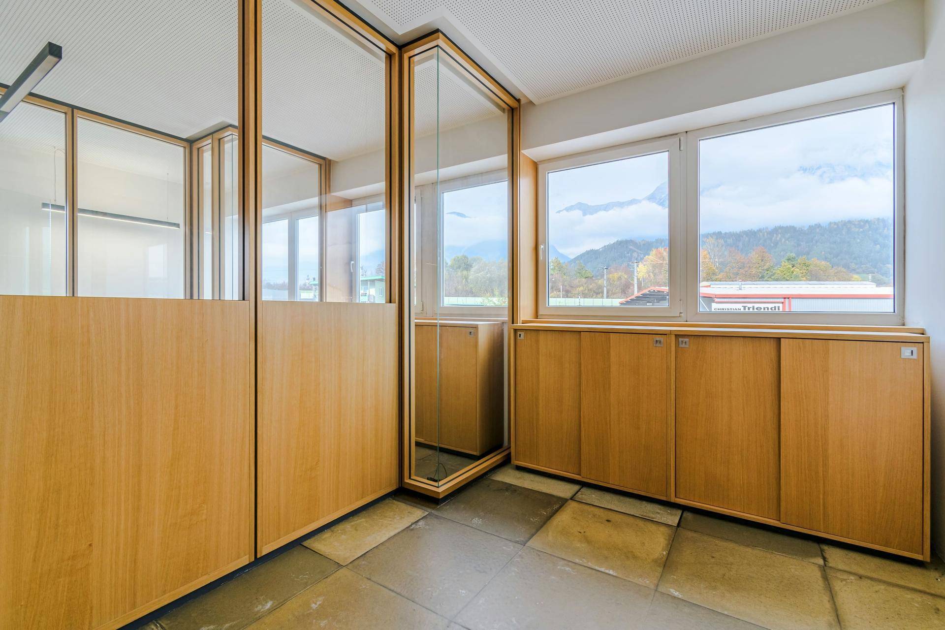 Büroraum mit großen Fenstern, die einen weiten Blick auf die Berge bieten, und Holzschränken.