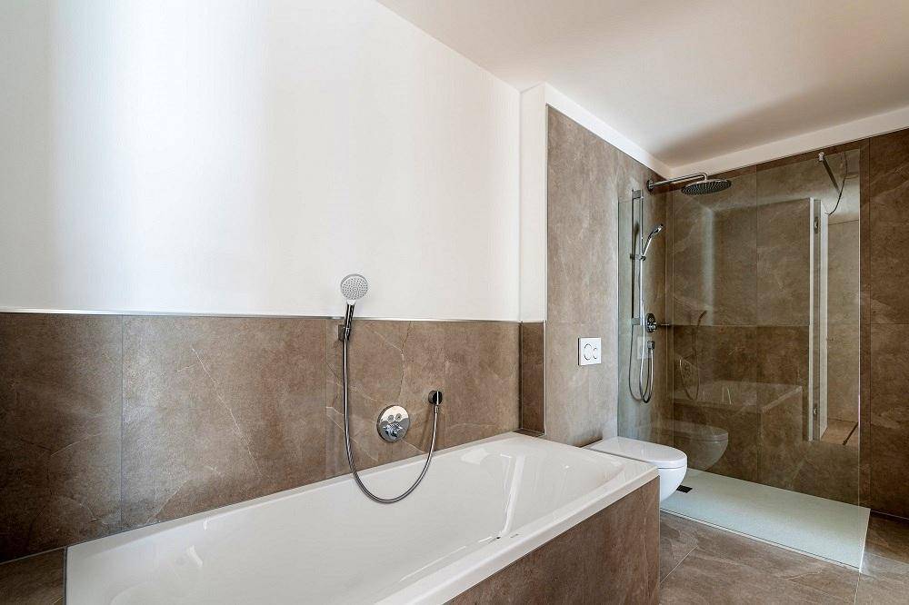 Modernes Badezimmer mit Badewanne, Dusche und eleganten braunen Fliesen an den Wänden.