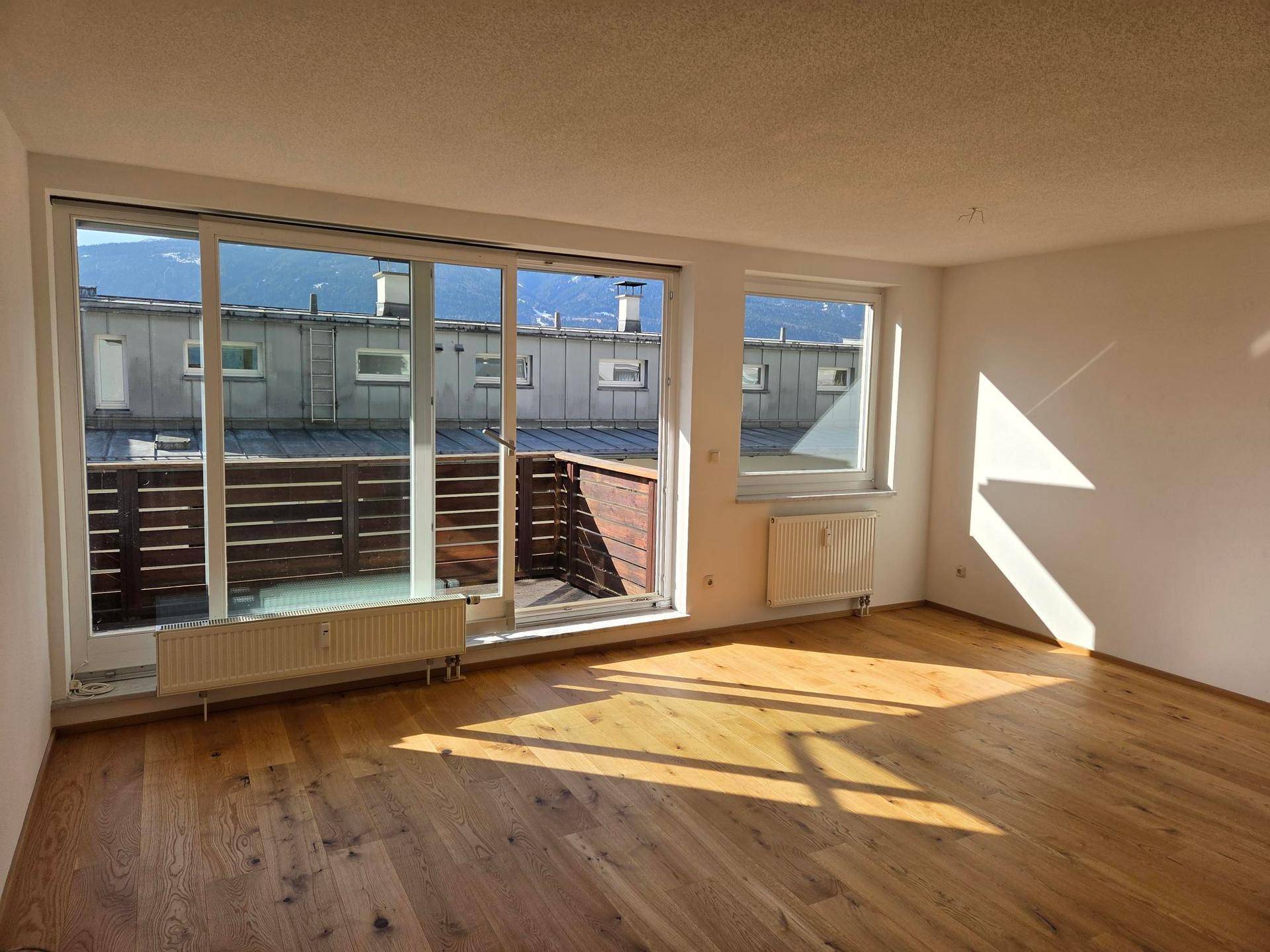 Lichtdurchflutetes Wohnzimmer mit Holzboden und Zugang zu einem Balkon mit Bergblick.
