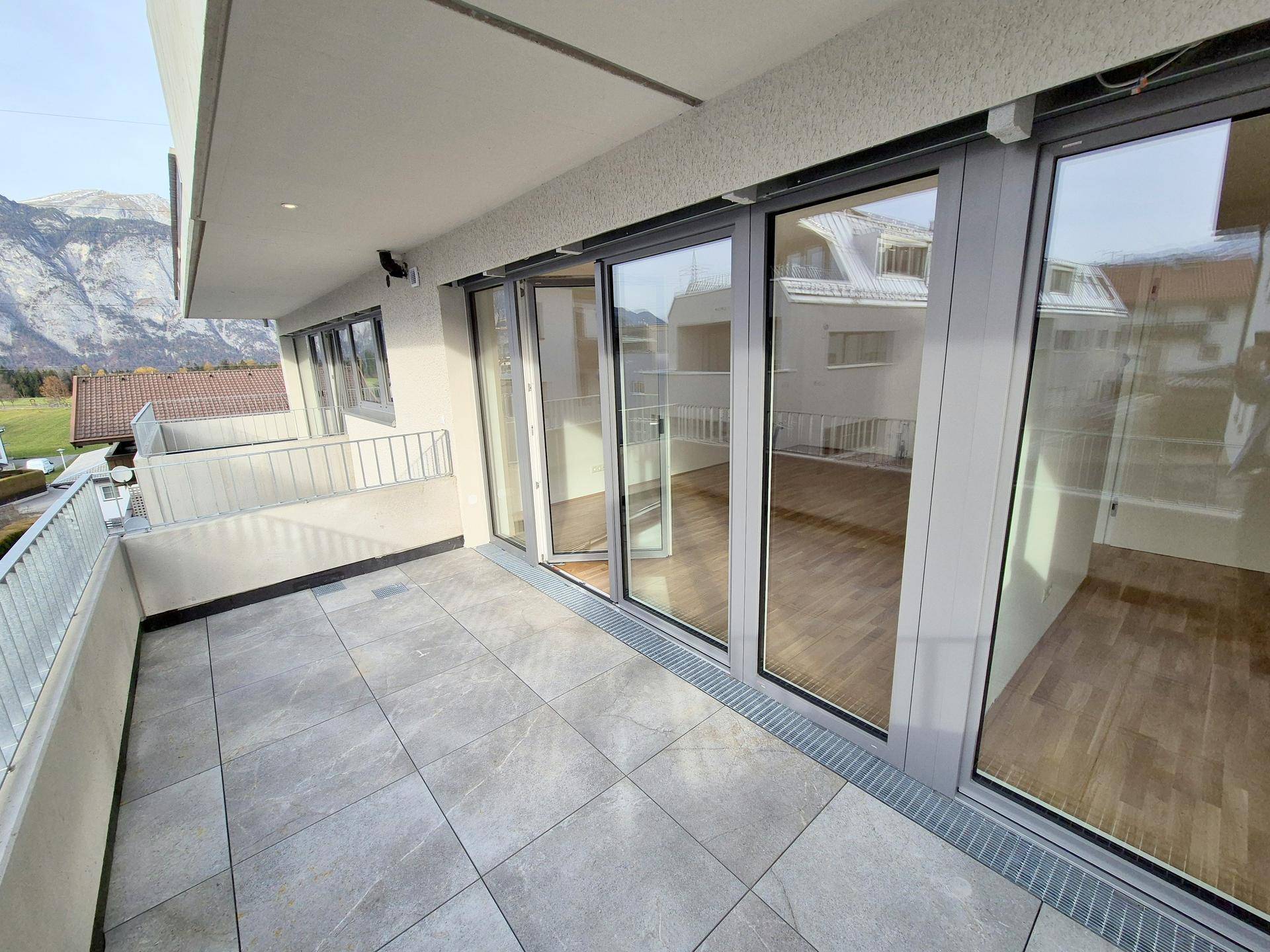 Heller Balkon mit großen Glasfronten und Fliesenboden, bietet Zugang zu den Innenräumen.
