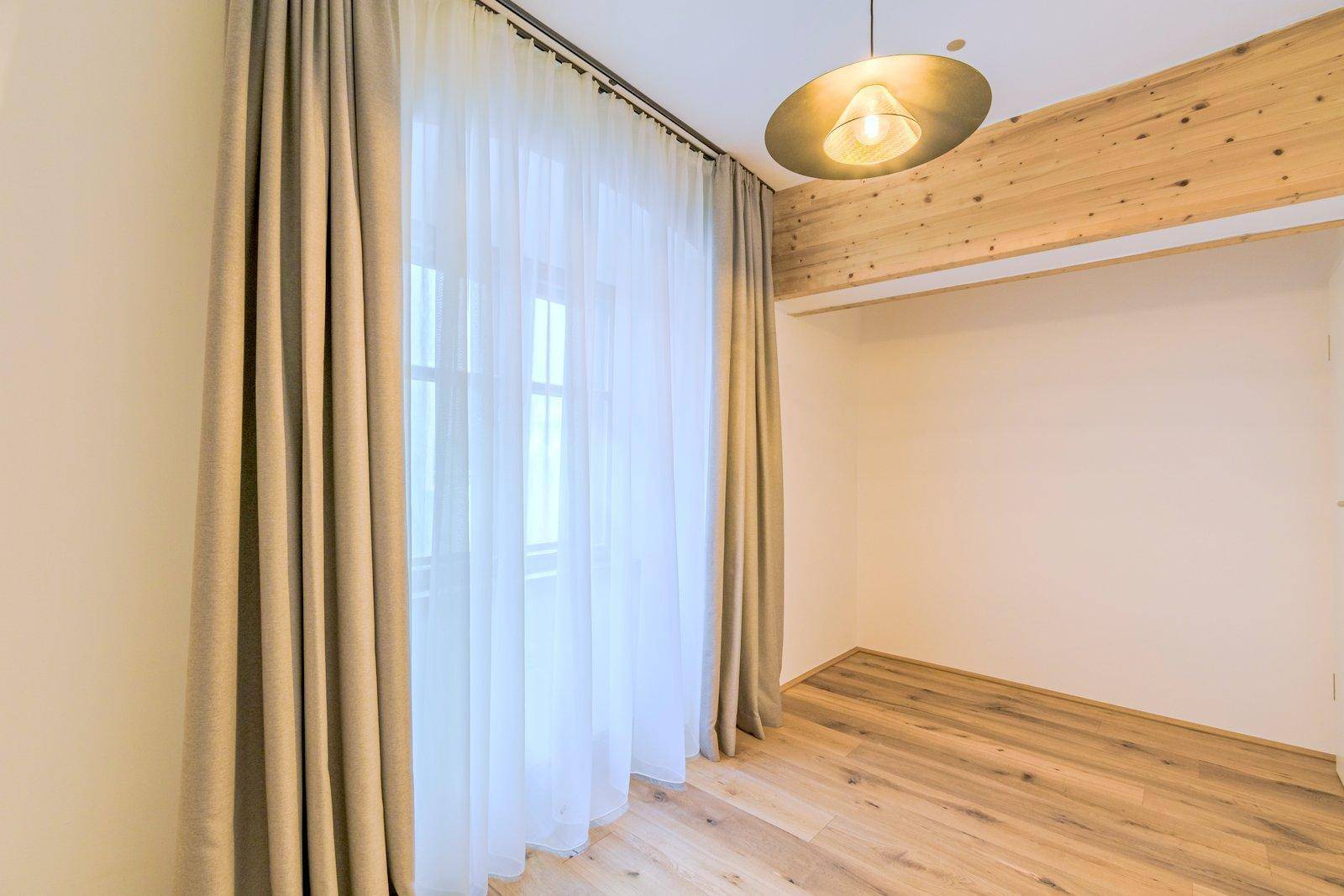 Helles Schlafzimmer mit Holzboden, einem großen Fenster und einem dekorativen Holzbalken.