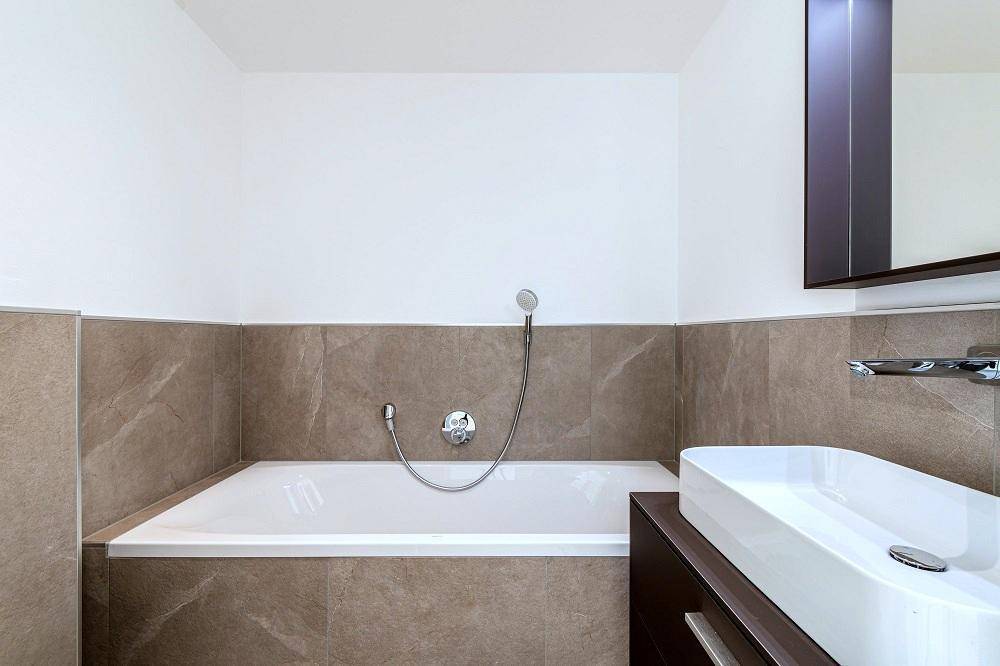 Elegantes Badezimmer mit integrierter Badewanne, modernem Waschtisch und hochwertigen Fliesen.