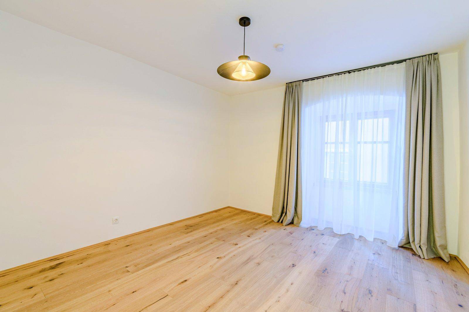 Helles Zimmer mit Holzboden und großen Fenstern, die viel Tageslicht hereinlassen.