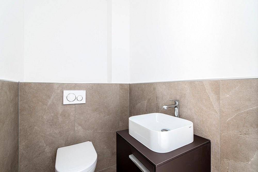 Modernes Gäste-WC mit Wand-WC und kleinem Waschbecken auf einem dunklen Unterschrank.