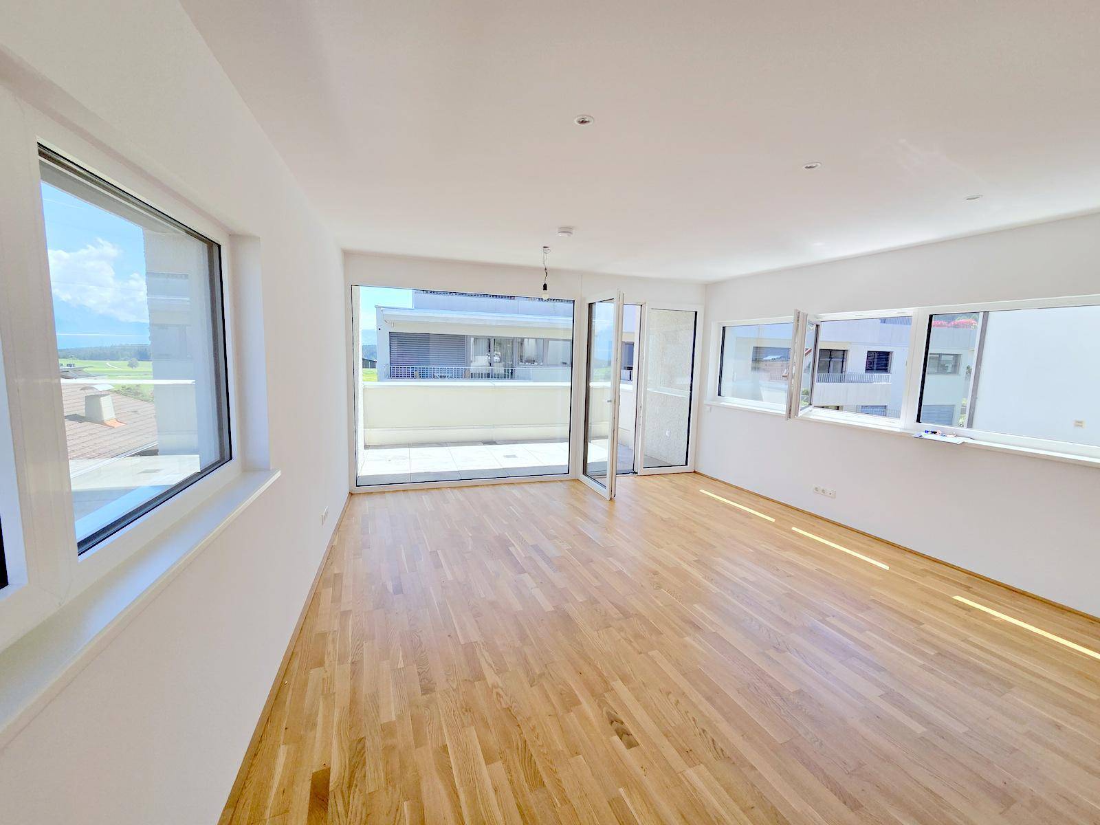 Heller Wohnraum mit Eichenparkettboden, großen Fenstern und Zugang zu einem Balkon.