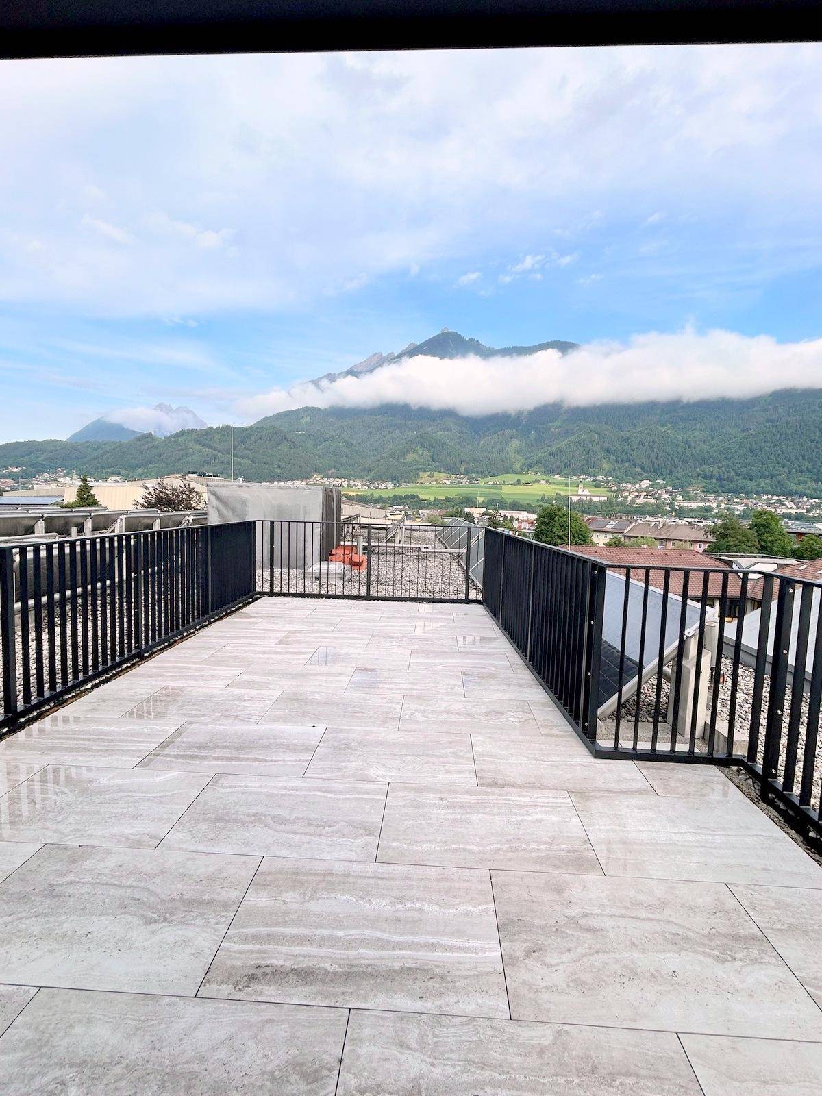 Geräumige Dachterrasse mit hellen Fliesen und beeindruckendem Bergblick unter bewölktem Himmel.