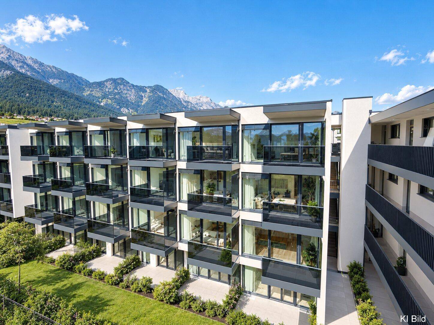 Moderne Wohnanlage mit zahlreichen Balkonen und großen Glasfronten vor alpiner Kulisse.