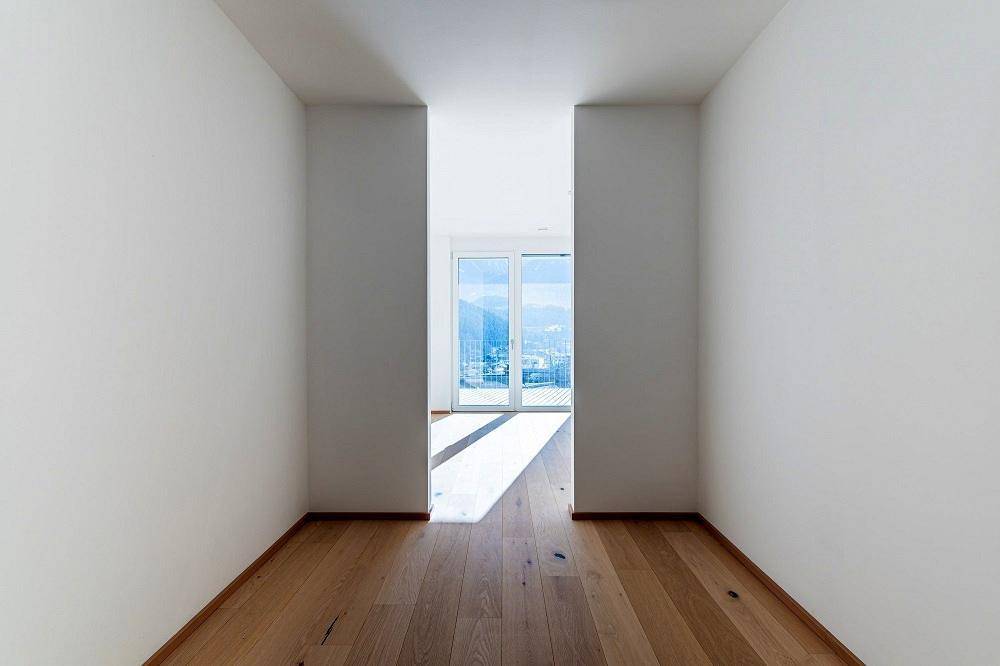 Heller Flur mit Holzboden, der zu einem Raum mit großen Fenstern und Bergblick führt.