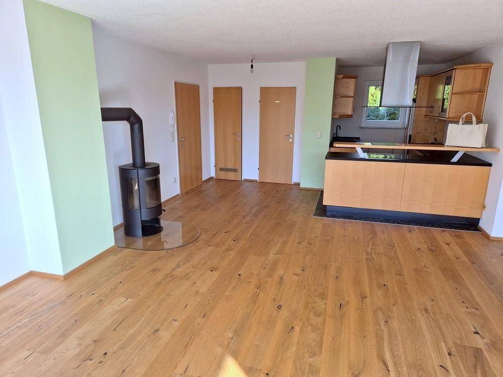 Heller offener Wohnbereich mit Holzboden, Kaminofen und integrierter Küchenzeile.