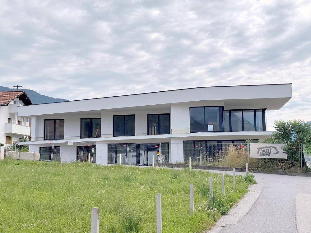 Zeitgenössisches weißes Gebäude mit klaren Linien und großen Fenstern, eingebettet in eine grüne Umgebung.