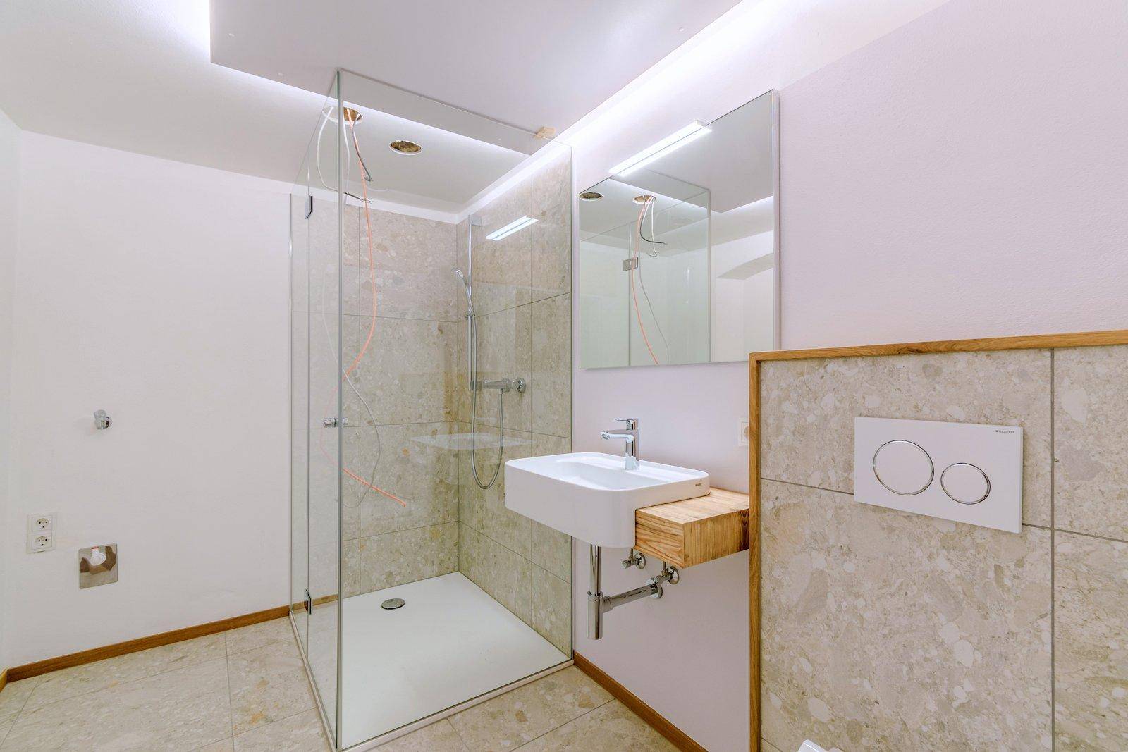Modernes Badezimmer mit begehbarer Dusche, eleganten Fliesen und einem Waschbecken mit Holzunterschrank.