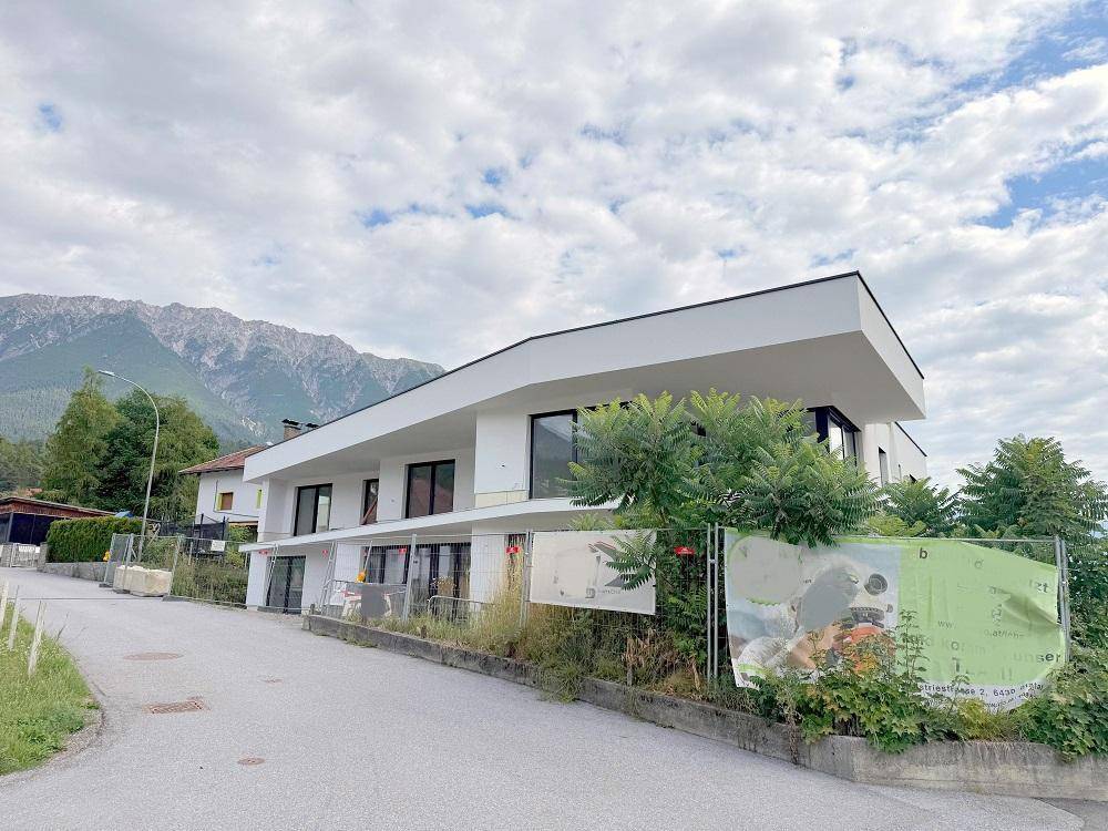 Moderner Neubau mit klaren Linien, großen Fenstern und einer malerischen Bergkulisse im Hintergrund.