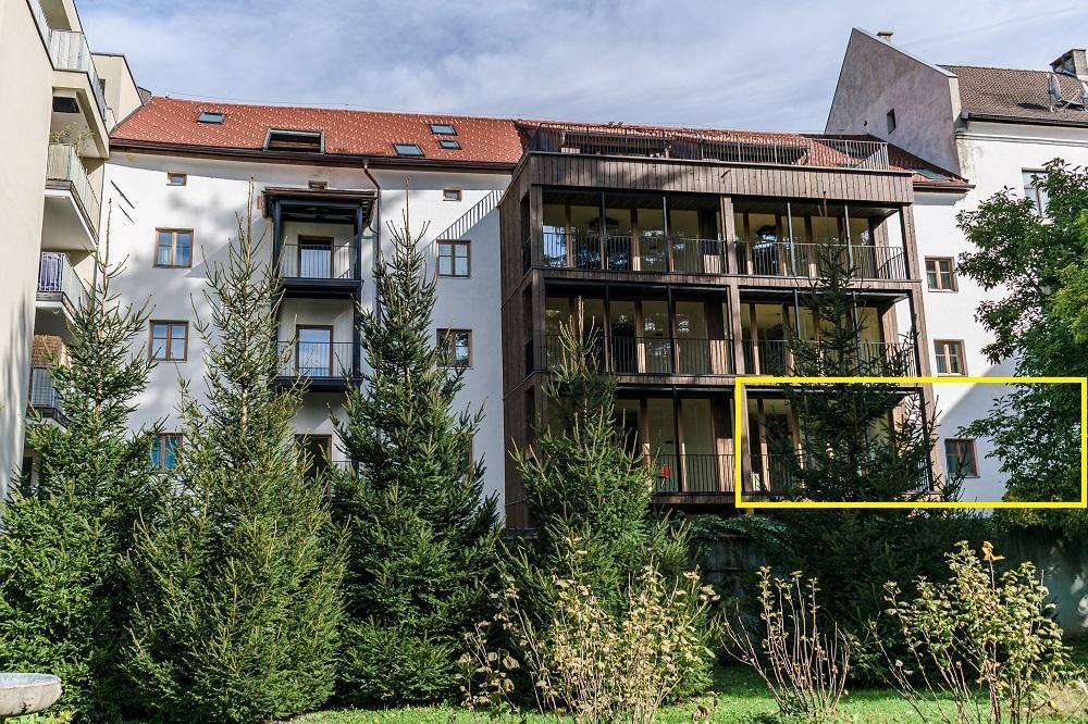 Moderne Gebäudefassade mit mehreren Balkonen und großen Fenstern, umgeben von üppigem Grün.