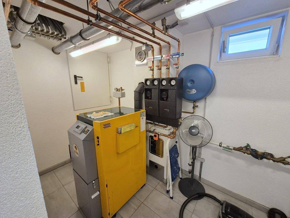 Heizungsraum mit moderner Anlage, sichtbaren Kupferrohren und kleinem Fenster.