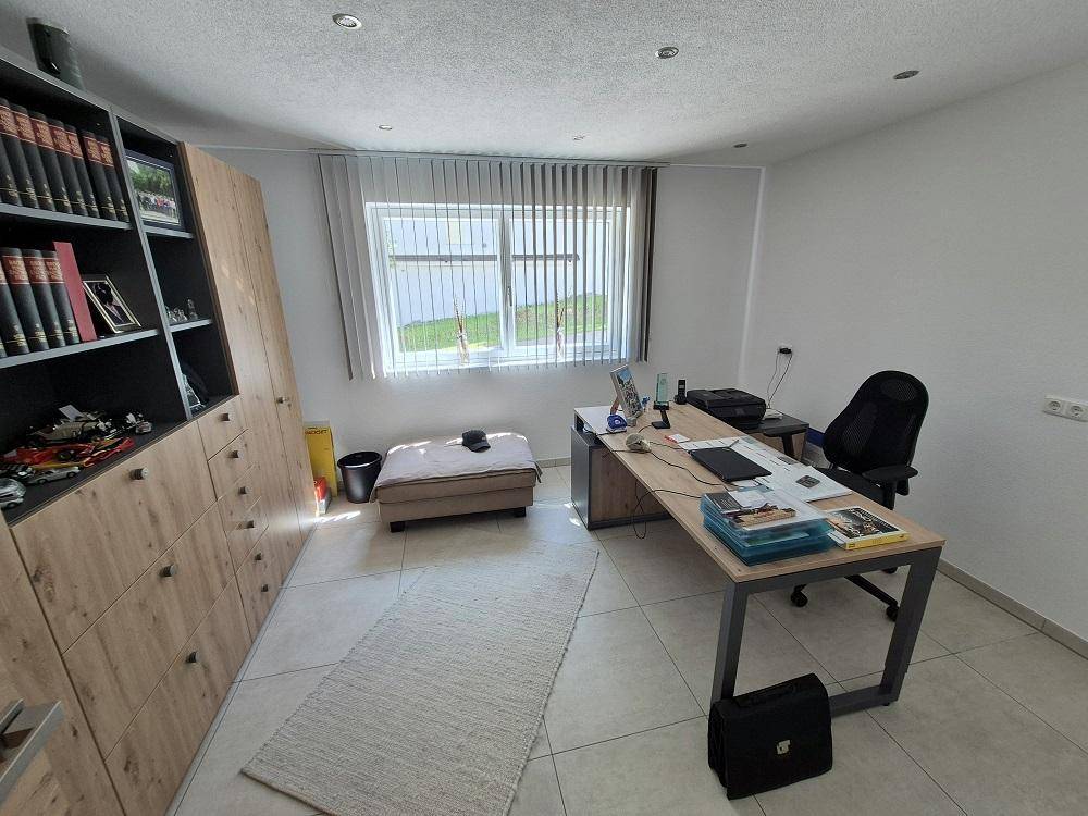 Geräumiges Büro mit großem Schreibtisch, Bücherregal und Fenster mit Blick ins Grüne.