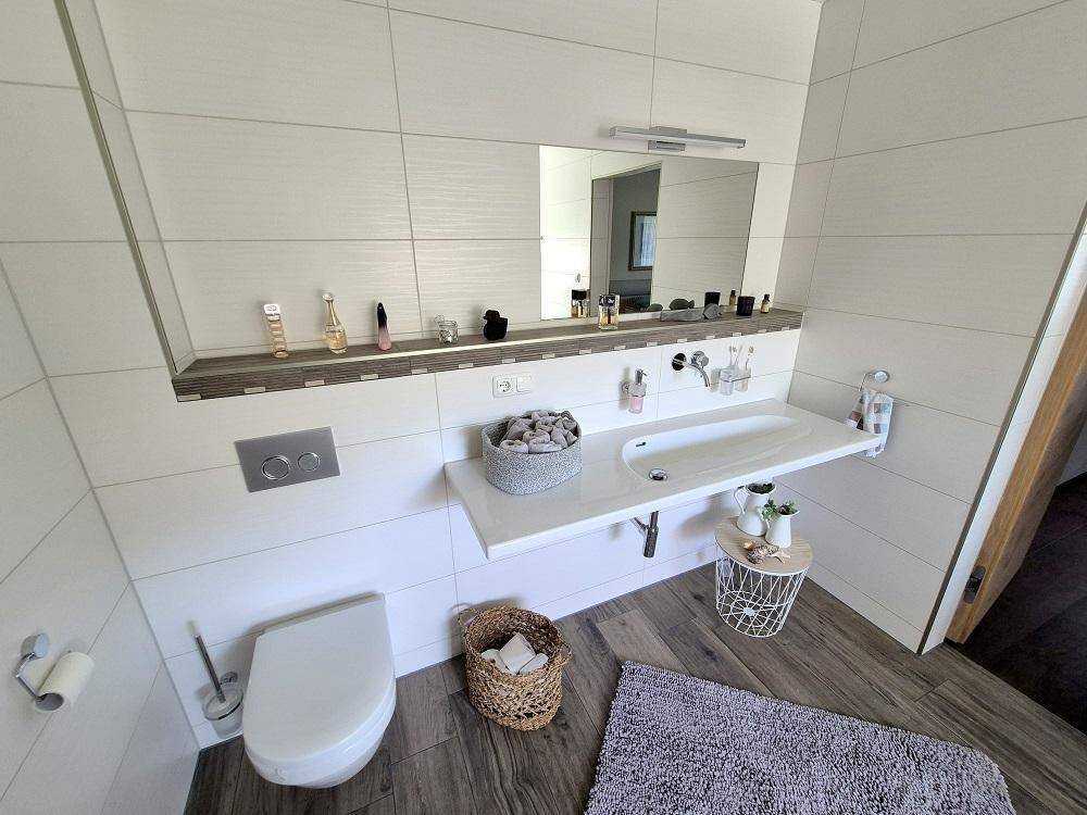 Modernes Gäste-WC mit Wand-WC, Einzelwaschbecken und Holzoptik-Fliesenboden.