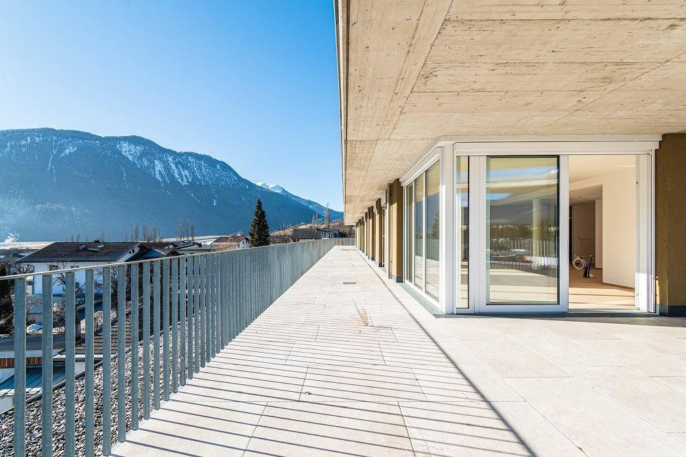 Langer Balkon oder Terrasse mit Fliesenboden und weitem Blick auf die schneebedeckten Berge.