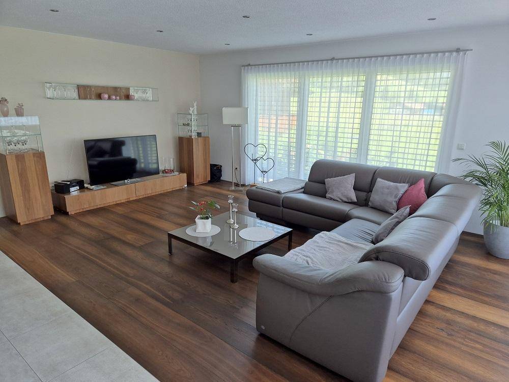 Gemütliches Wohnzimmer mit großem Sofa, Holzboden und Zugang zur Terrasse durch große Fenster.