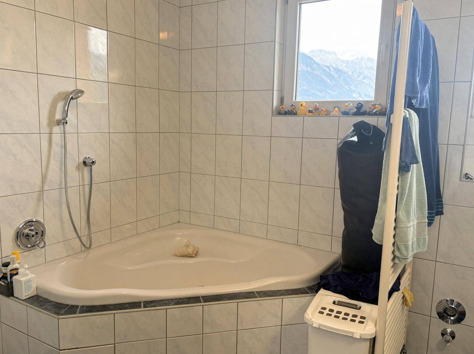 Badezimmer mit einer Eckbadewanne, Duschfunktion und weißen Wandfliesen.