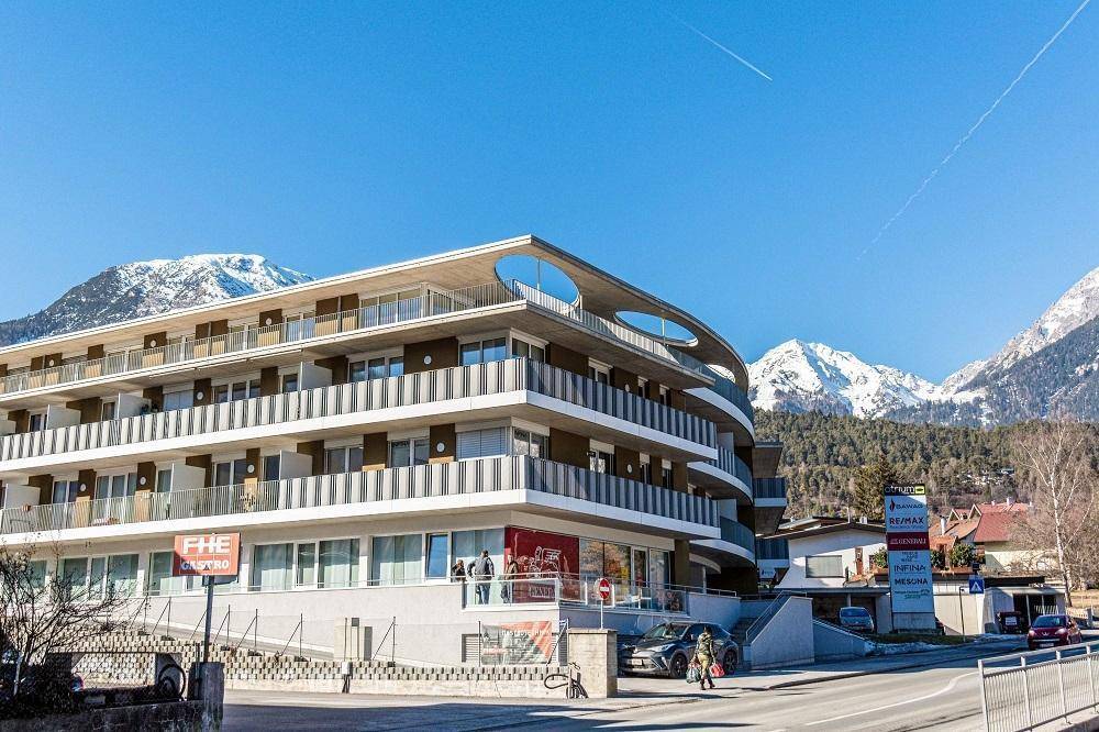 Weitläufige Ansicht des modernen Gebäudes mit Geschäften im Erdgeschoss und Bergpanorama.