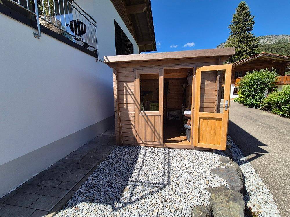 Kleiner Holzschuppen auf einem Kiesbereich neben dem Haus, ideal für Gartengeräte.