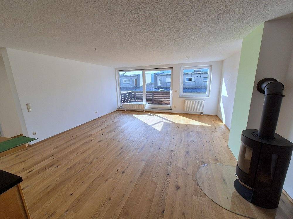 Heller Wohnbereich mit Kaminofen, Holzboden und großen Fenstern, die viel Tageslicht hereinlassen.