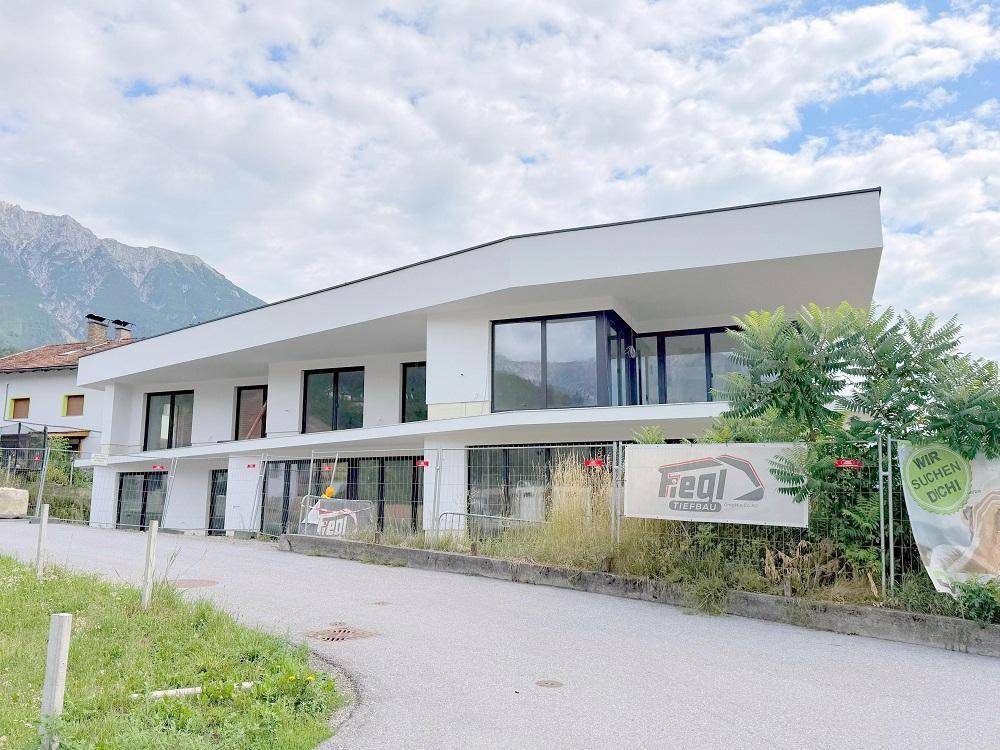 Neubau mit moderner Architektur und großen Fensterflächen vor alpiner Kulisse.