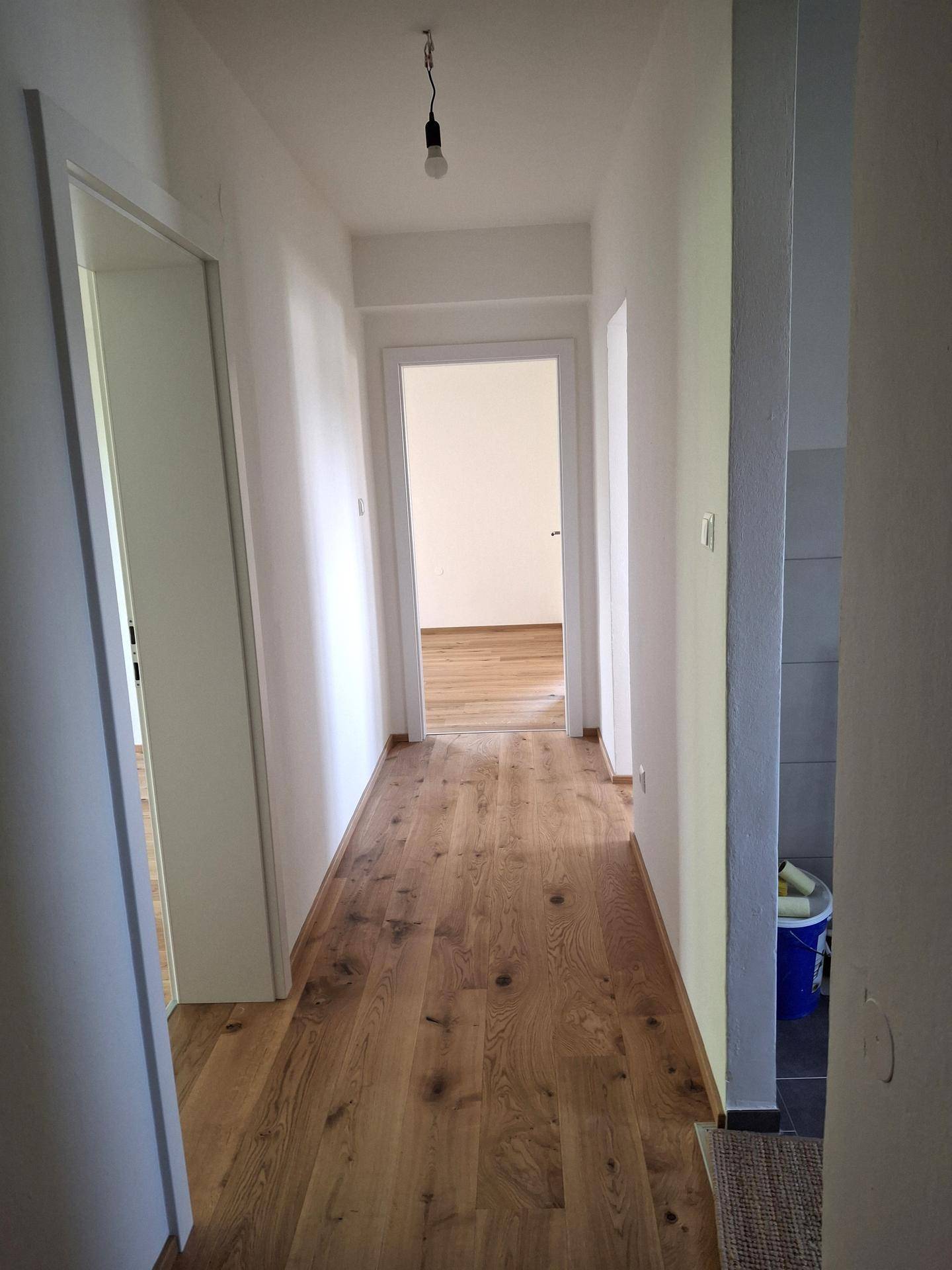 Heller Flur mit Holzboden und weißen Wänden, der zu weiteren Zimmern der Wohnung führt.