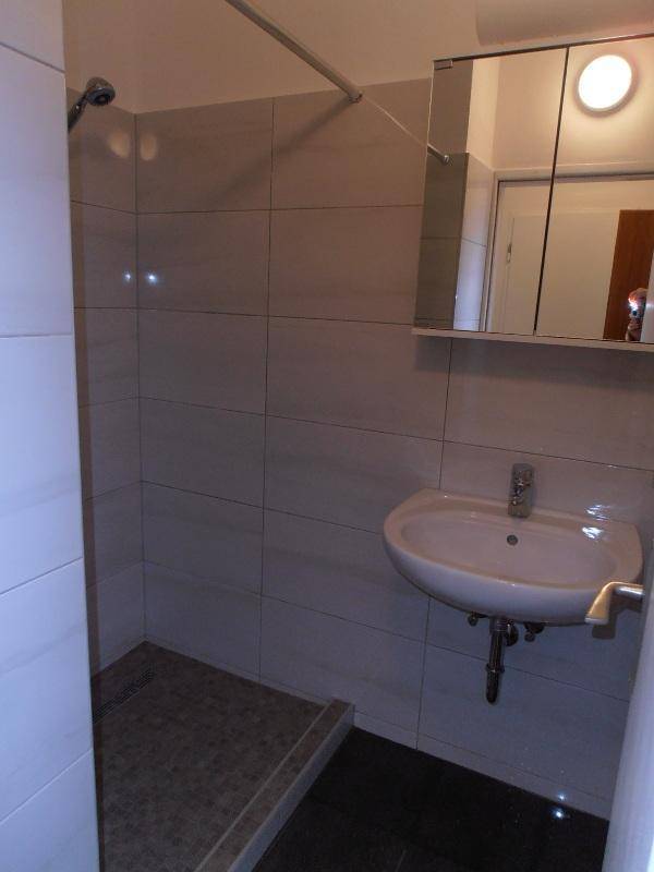 Modernes Badezimmer mit Dusche, Waschbecken und Spiegelschrank, hell gefliest.
