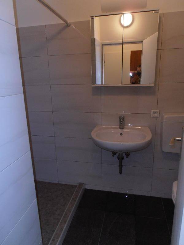 Helles Badezimmer mit Duschbereich, Waschbecken, Spiegelschrank und WC.
