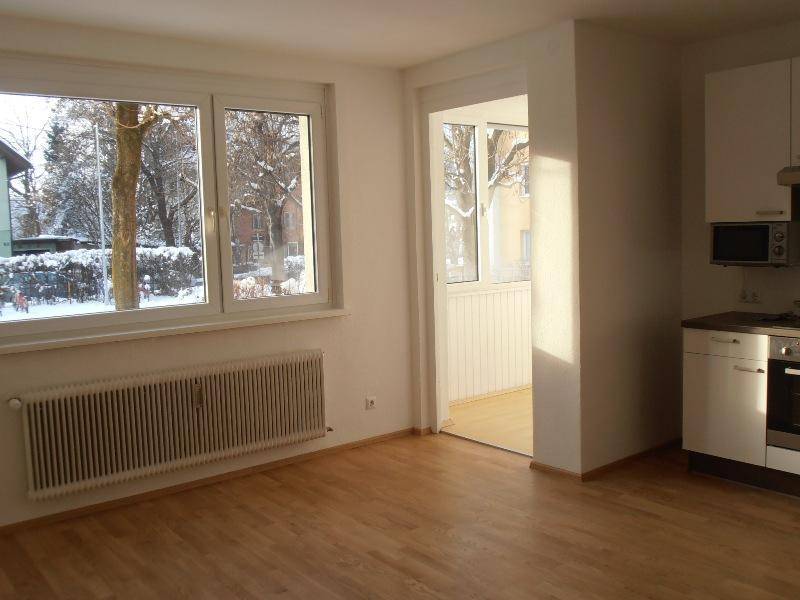 Heller Wohnbereich mit großen Fenstern, Holzboden und Zugang zu einem Balkon.