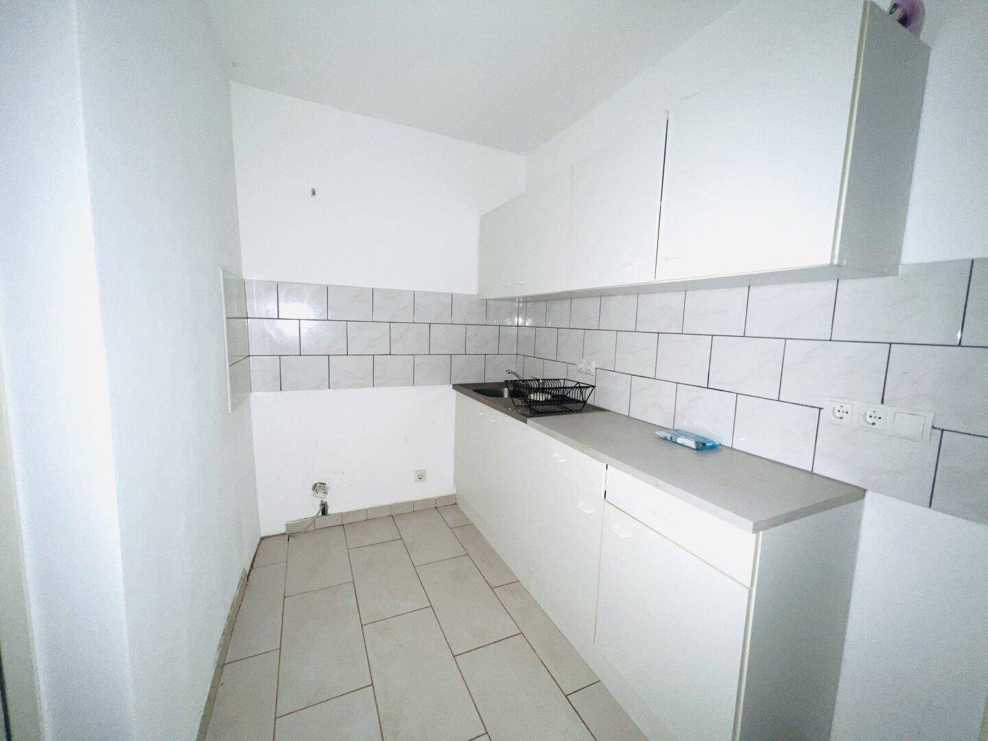 Einfache Küche mit weißen Schränken, Fliesenrückwand und hellem Fliesenboden.