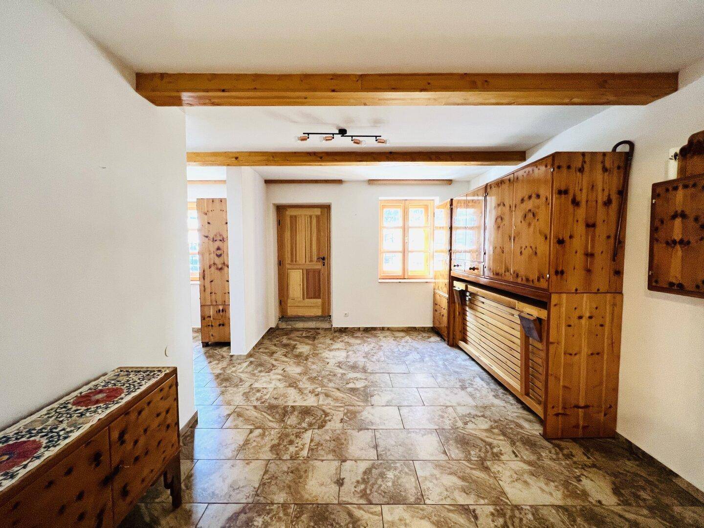 Heller Eingangsbereich mit Fliesenboden, sichtbaren Holzbalken und traditionellen Holzschränken.