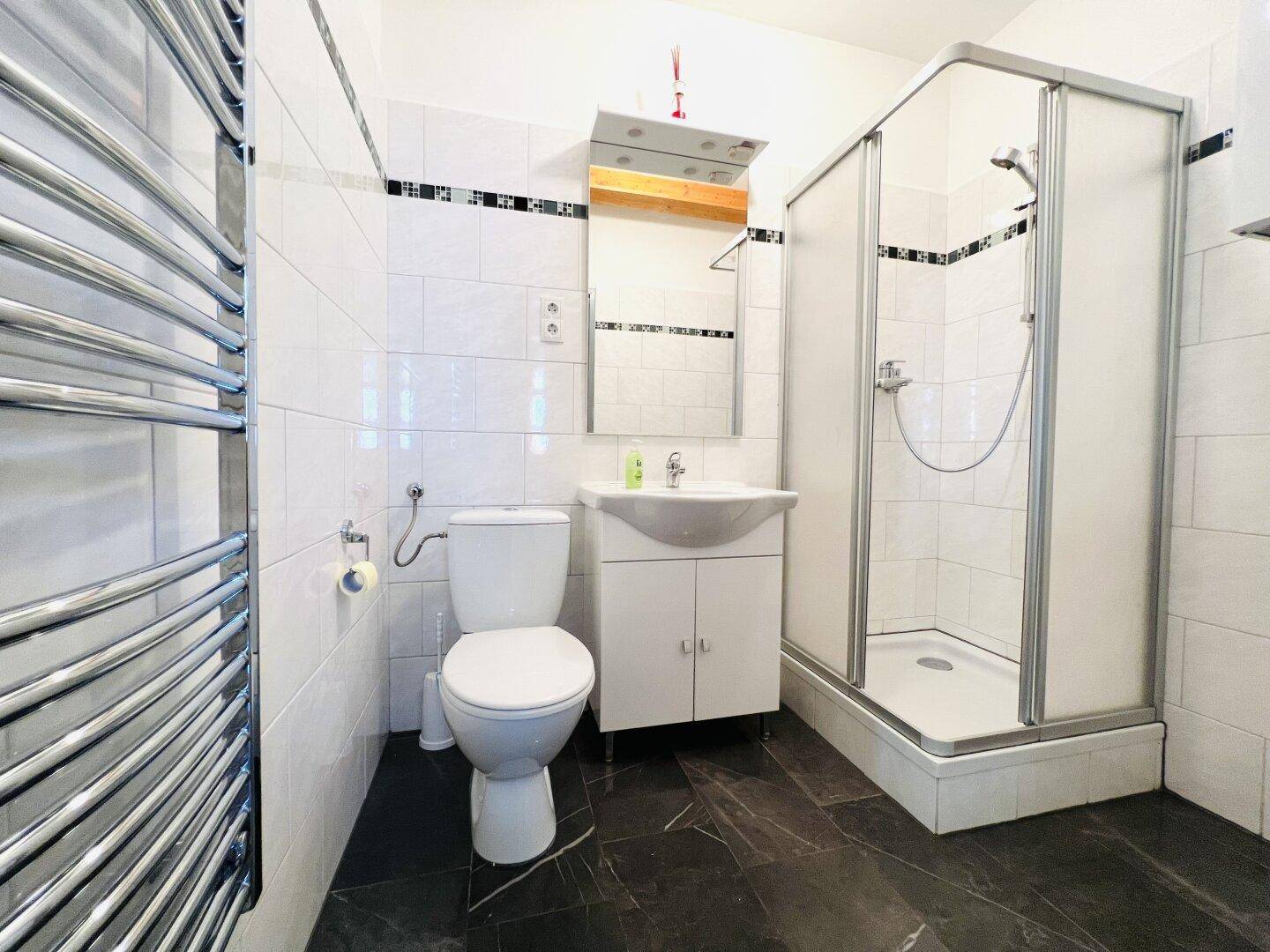 Modernisiertes Badezimmer mit Duschkabine, beheiztem Handtuchhalter und dunklem Fliesenboden.