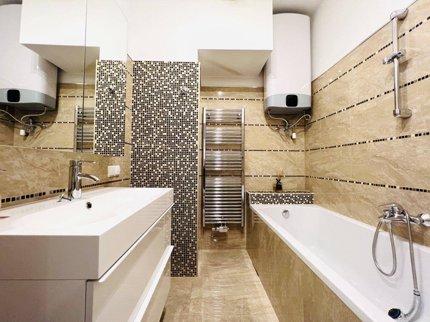 Elegantes Badezimmer mit beigefarbenen Fliesen, Badewanne und modernem Waschtisch.