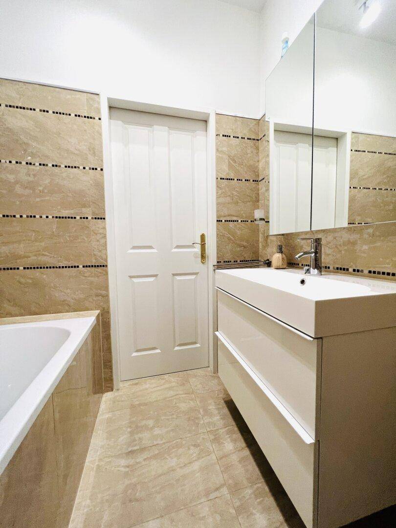 Modernes Badezimmer mit beigefarbenen Fliesen, Waschtisch und Spiegelschrank.
