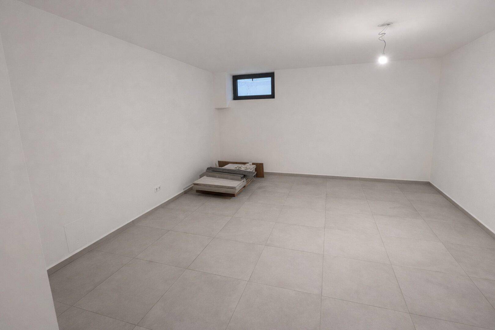 Geräumiger Kellerraum mit Fliesenboden und kleinem Fenster.