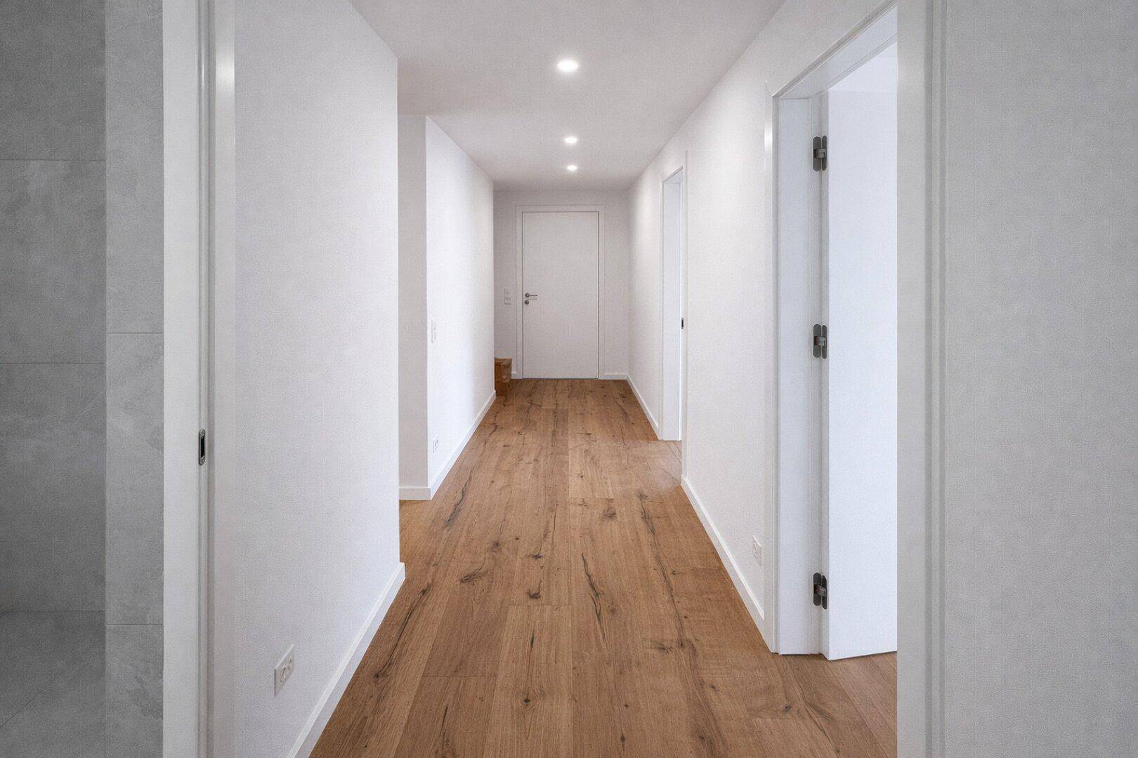 Langer, heller Flur mit Holzboden und modernen Einbaustrahlern in der Decke.