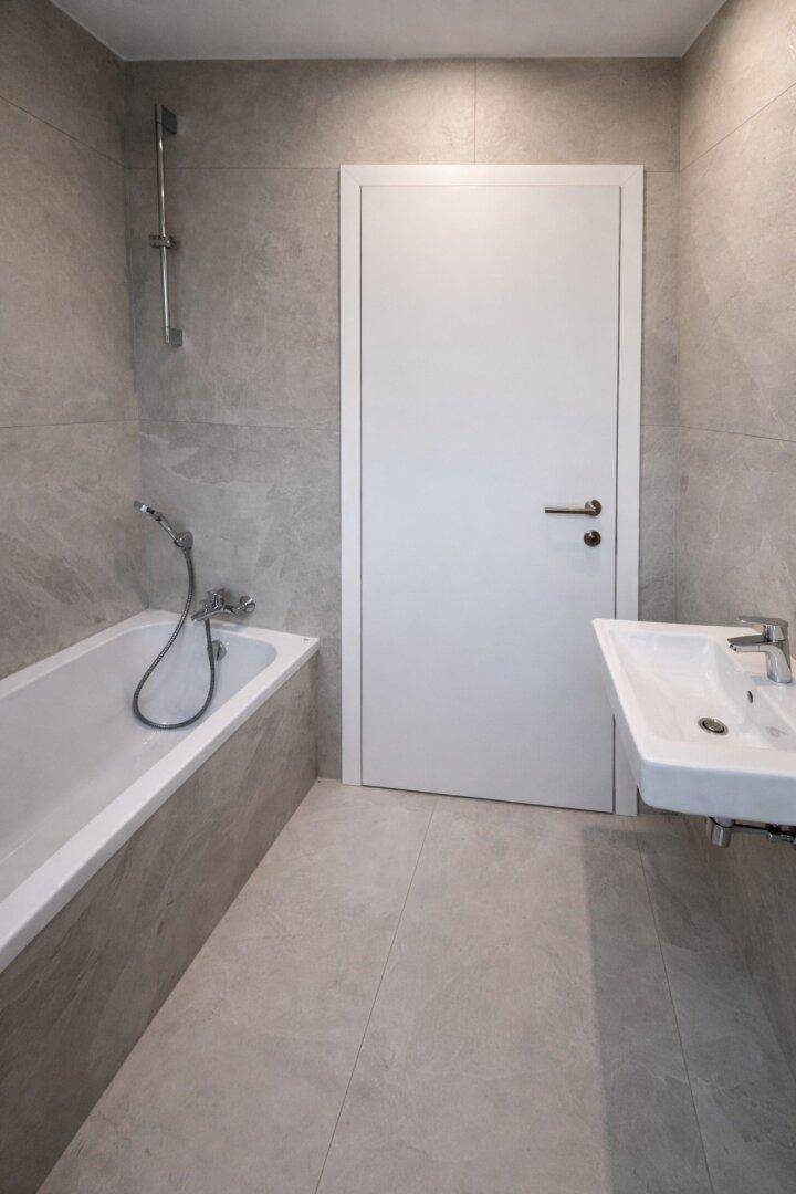 Modernes Badezimmer mit grauen Fliesen, Badewanne und einem Waschbecken mit Armatur.